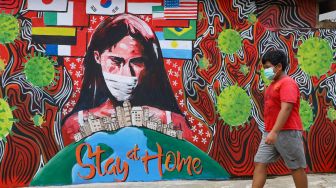 Seorang anak melintas didepan mural "Stay At Home" bertemakan virus Corona di Cipayung, Depok, Jawa Barat, Rabu (15/4). [Suara.com/Alfian Winanto]
