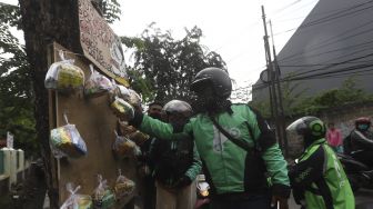 Pengemudi ojek online mengambil paket bahan makanan yang digantung oleh seniman wayang uwuh Iskandar Hardjodimuljo di salah satu pohon kawasan jalan Cawang Baru Utara, Jakarta Timur, Sabtu (18/4). [Suara.com/Angga Budhiyanto]