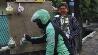 Pengemudi ojek online mengambil paket bahan makanan yang digantung oleh seniman wayang uwuh Iskandar Hardjodimuljo di salah satu pohon kawasan jalan Cawang Baru Utara, Jakarta Timur, Sabtu (18/4). [Suara.com/Angga Budhiyanto]