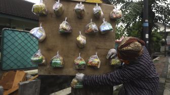 Seniman wayang uwuh Iskandar Hardjodimuljo menggantungkan sumbangan paket bahan makanan di salah satu pohon kawasan jalan Cawang Baru Utara, Jakarta Timur, Sabtu (18/4). [Suara.com/Angga Budhiyanto]