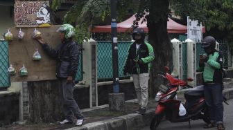 Pengemudi ojek online mengambil paket bahan makanan yang digantung oleh seniman wayang uwuh Iskandar Hardjodimuljo di salah satu pohon kawasan jalan Cawang Baru Utara, Jakarta Timur, Sabtu (18/4). [Suara.com/Angga Budhiyanto]