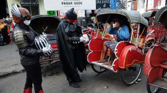 Warga menggunakan kostum superhero Gundala dan Batman membagikan masker kain kepada sejumlah pekerja yang beraktivitas di Pasar Gede, Solo, Minggu (19/4).  [ANTARA FOTO/Maulana Surya]
