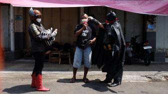Warga menggunakan kostum superhero Gundala dan Batman bagikan masker kain kepada sejumlah pekerja yang beraktivitas di Pasar Gede, Solo, Minggu (19/4).  [ANTARA FOTO/Maulana Surya]