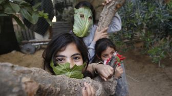 Tiga anak berpose dengan masker yang terbuat dari daun kubis ditengah wabah virus Corona, di Beit Lahia, Jalur Gaza, Palestina, Kamis (16/4/2020).  (AFP/Mohamed Abed)