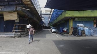 Pedagang melintas di pasar Tanah Abang yang sepi pengunjung pada hari kedua di bulan suci Ramadhan akibat pandemi virus Corona (COVID-19) di Jakarta, Minggu (26/4). [Suara.com/Angga Budhiyanto]