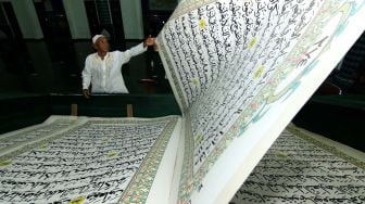 Seorang umat Islam membalik halaman saat tadarus membaca Al Quran raksasa di Masjid Baiturrahman, Banyuwangi, Jawa Timur, Senin (27/4).   [ANTARA FOTO/Budi Candra Setya]