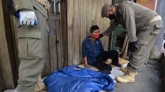 Petugas Satpol PP membangunkan seorang pengemis yang tidur di emperan toko di Jalan Dewi Sartika, Cawang, Jakarta, Rabu (29/4). [ANTARA FOTO/Aditya Pradana Putra]