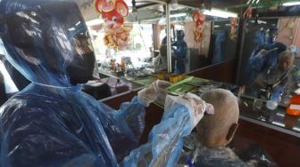 Tukang Cukur Gunakan Jas Hujan Sebagai APD