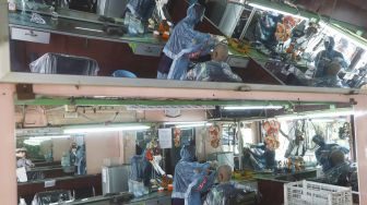 Tukang cukur menggunakan APD (Alat Pelindung Diri) saat mencukur pelanggan di kawasan Pondok Kelapa, Jakarta Timur, Selasa (5/5). Suara.com/Angga Budhiyanto]