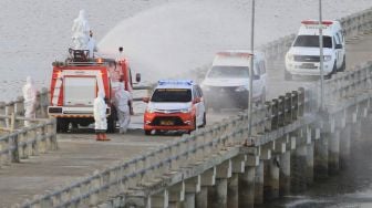 Petugas menyemprotkan cairan ke mobil ambulans yang mengangkut pasien positif COVID-19 dari Kabupaten Simeulue di Pelabuhan Penyeberangan Meulaboh-Sinabang Desa Gampong Teungoh, Samatiga, Aceh Barat, Aceh, Rabu (13/5).  [ANTARA FOTO/Syifa Yulinnas]