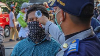 Petugas mengecek suhu tubuh pengendara sepeda motor yang akan memasuki Bekasi dengan Thermo Gun di Check Point PSBB Pondok Gede, Bekasi, Jawa Barat, Kamis (15/5). [Suara.com/Alfian Winanto]