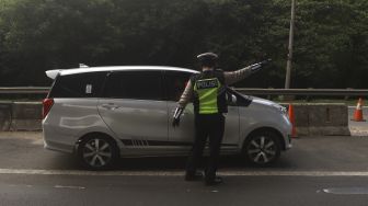 Petugas Kepolisian mengarahkan kendaraan untuk keluar dari Tol Jakarta-Cikampek, Cikarang Barat, Kabupaten Bekasi, Jawa Barat, Rabu (20/5). [Suara.com/Angga Budhiyanto]  