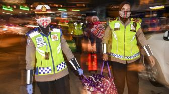 Petugas kepolisian membantu membawakan barang-barang milik calon pemudik yang terjaring razia penyekatan di Pintu Tol Cikarang Barat, Bekasi, Jawa Barat, Kamis (21/5/2020). [ANTARA FOTO/Nova Wahyudi]
