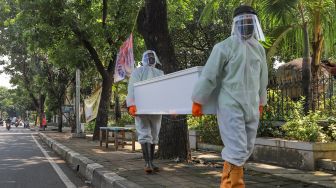 Petugas tempat pemakaman umum (TPU) membawa peti mati  di TPU Tanah Kusir, Jakarta Selatan, Sabtu (23/5). [Suara.com/Alfian Winanto]
