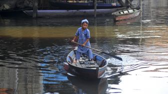 Seorang anak menggunakan perahu melintasi jalan permukiman yang terendam banjir luapan Sungai Batanghari saat perayaan Idul Fitri 1441 Hijriah di Tahtul Yaman, Pelayangan, Jambi, Minggu (24/5). [ANTARA FOTO/Wahdi Septiawan]