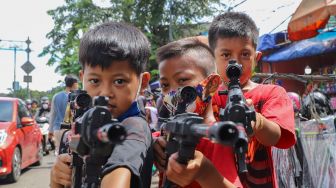 Anak-anak mencoba mainan tembak-tembakan yang baru saja dibelinya di Pasar Gembrong, Jakarta Timur, Selasa (26/5). [Suara.com/Alfian Winanto]
