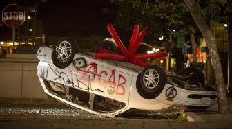 Sebuah mobil dirusak terbalik ketika pengunjuk rasa berhadapan dengan polisi di Oakland, California, Jumat (29/5). [Josh Edelson / AFP]