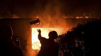 Seorang demonstran melemparkan alat pemadam kebakaran ke gedung yang terbakar saat demonstrasi di Minneapolis, Minnesota, Jumat (29/5). [Chandan Khanna/ AFP]