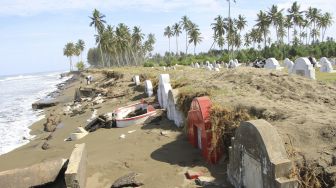 Warga melintas di samping makam etnis Tionghoa yang rusak akibat gelombang pasang di Desa Suak Ribee, Kecamatan Johan Pahlawan, Aceh Barat, Aceh, Sabtu (30/5). [ANTARA FOTO/Syifa Yulinnas]