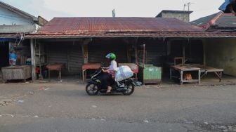 Pedagang melintas didepan  deretan warung tutup di Pasar Cisalak, Depok, Jawa Barat, Minggu (31/5). [Suara.com/Alfian Winanto]