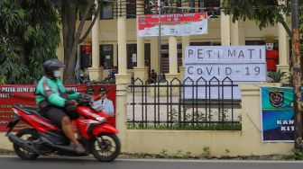 Pengemudi ojol melintas di depan peti mati Covid-19 di Kantor Kecamatan Sawangan, Depok, Jawa Barat, Senin (1/6). [Suara.com/Alfian Winanto]