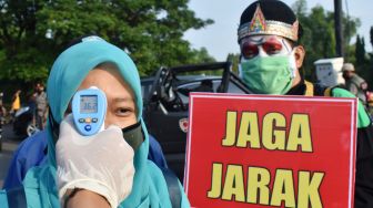 Petugas memeriksa suhu tubuh pengunjung di jalan masuk kawasan hari bebas kendaraan bermotor atau 'car free day' Taman Lalu Lintas Bantaran Sungai Madiun di Kota Madiun, Jawa Timur, Minggu (7/6). [ANTARA FOTO/Siswowidodo]