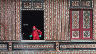 Petugas memberikan disinfektan pada bangunan rumah Gadang di Anjungan Sumatra Barat, Taman Mini Indonesia Indah, Jakarta Timur, Rabu (10/6). [Suara.com/Alfian Winanto]
