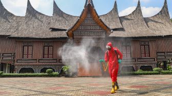 Petugas melakukan penyemprotan disinfektan di halam rumah Gadang di Anjungan Sumatra Barat, Taman Mini Indonesia Indah, Jakarta Timur, Rabu (10/6). [Suara.com/Alfian Winanto]