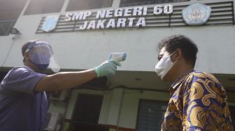 Petugas memindai suhu tubuh seorang tamu dalam simulasi pendaftaran di posko PPDB SMP Negeri 60, Kecamatan Gambir, Jakarta Pusat, Rabu (10/6). [Suara.com/Angga Budhiyanto]