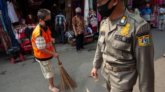 Petugas Satpol PP mengawasi pelanggar aturan pembatasan sosial berskala besar (PSBB) yang melaksanakan sanksi kerja sosial di Pasar Jatinegara, Jakarta, Kamis (11/6/2020). [ANTARA FOTO/Aditya Pradana Putra]