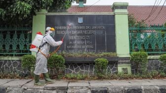 Petugas PMI menyemprotkan disinfektan area luar  SDN 01 Menteng, Jakarta Pusat, Senin (15/1). [Suara.com/Alfian Winanto]