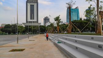 Pekerja melintas di deretan tribun tempat duduk di area revitalisasi Monas, Jakarta Pusat, Kamis (18/6). [Suara.com/Alfian Winanto]