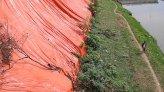 Warga melintas dibawah area longsor di pinggir Banjir Kanal Timur (BKT), Malaka Sari, Jakarta Timur, Jumat (19/6). [Suara.com/Alfian Winanto]