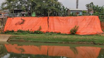 Penampakan terpal besar yang menutupi lokasi tanah longsor di pinggir Banjir Kanal Timur (KBT), Malaka Sari, Jakarta Timur, Jumat (19/6). [Suara.com/Alfian Winanto