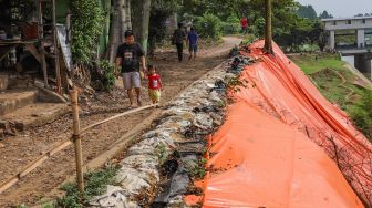 Warga melintas di area longsor pinggir Banjir Kanal Timur (BKT), Malaka Sari, Jakarta Timur, Jumat (19/6). [Suara.com/Alfian Winanto]