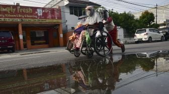 Seorang penyandang disabilitas, Yanti (34) duduk di atas kursi roda dan didorong anaknya saat berjualan makanan di jalanan Kota Pekanbaru, Riau, Sabtu (20/6). [ANTARA FOTO/FB Anggoro]