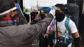 Petugas memeriksa suhu tubuh calon pendaki di pintu gerbang jalur pendakian Gunung Lawu di Cemoro Sewu, Magetan, Jawa Timur, Sabtu (27/6/2020). [ANTARA FOTO/Siswowidodo]