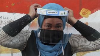 Pedagang memakai alat pelindung wajah (face shield) yang didapat dari pembagian Alat Pelindung Diri (APD) di Pasar Keputih, Surabaya, Jawa Timur, Minggu (28/6). [ANTARA FOTO/Didik Suhartono]