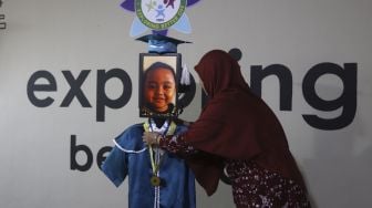 Kepala Sekolah mengalungkan piagam tanda kelulusan kepada siswa Kelompok Bermain Taman Kanak-kanak (KB TK) saat wisuda virtual menggunakan Roboda (Robot Wisuda) di Sekolah Nasional Satu (Nassa School), Bekasi, Jawa Barat, Rabu (1/7) . [Suara.com/Angga Budhiyanto]
