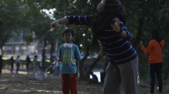 Dua anak bermain bulutangkis saat Hari Bebas Kendaraan Bermotor (HBKB) atau Car Free Day (CFD) di kawasan Banjir Kanal Timur (BKT), Duren Sawit, Jakarta, Minggu (5/7). [Suara.com/Angga Budhiyanto] 