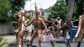 Anak-anak bermain di dekat patung-patung yang menggambarkan nasib orang-orang yang tidak menjujung tinggi lima ajaran Budhha di sebuah taman yang menggambrakan neraka versi Budhha di Kuil Wat Saeng Suk di Provinsi pantai Thailand Chonburi (9/7/2020). [Lillian SUWANRUMPHA / AFP]