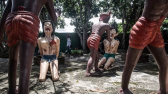 Seorang wanita berjalan di dekat patung-patung yang menggambarkan nasib orang-orang yang tidak menjujung tinggi lima ajaran Budhha di sebuah taman yang menggambrakan neraka versi Budhha di Kuil Wat Saeng Suk di Provinsi pantai Thailand Chonburi (9/7/2020). [Lillian SUWANRUMPHA / AFP]
