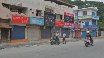 Warga berdiri di depan toko-toko yang tutup saat pemberlakuan lockdown di Bangolore, India, Rabu (15/7).  [Manjunath Kiran/AFP]