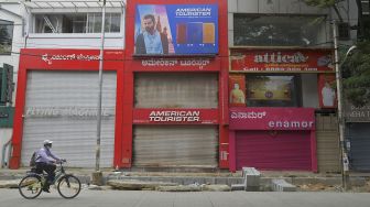 Seorang pria menggunakan sepeda melintas di depan toko-toko yang tutup saat pemberlakuan lockdown di Bangolore, India, Rabu (15/7). [Manjunath Kiran/AFP]