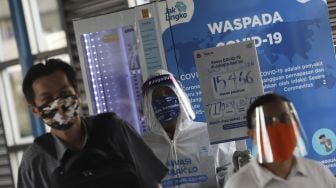 Anggota komunitas pecinta Transjakarta mengenakan baju hazmat dengan membawa poster berisi informasi jumlah kasus positif di Jakarta saat melakukan sosialisasi protokol kesehatan di Halte Transjakarta Harmoni, Jakarta, Jumat (17/7/2020). [Suara.com/Angga Budhiyanto]