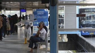 Anggota komunitas pecinta Transjakarta mengenakan baju hazmat dengan membawa poster berisi informasi jumlah kasus positif di Jakarta saat melakukan sosialisasi protokol kesehatan di Halte Transjakarta Harmoni, Jakarta, Jumat (17/7/2020). [Suara.com/Angga Budhiyanto]