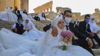 Sejumlah pasangan pengantin mengenakan masker wajah duduk di tangga selama acara pernikahan bersama di tengah pandemi Covid-19 di Kuil Bacchus di situs bersejarah Baalbek di Lembah Bekaa, Lebanon Timur, Jumat (24/7/2020). [AFP]