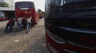 Sejumlah mekanik mendorong bus di salah satu pool bus pariwisata di kawasan Tanjung Barat, Jagakarsa, Jakarta, Selasa (28/7/2020). [Suara.com/Angga Budhiyanto]