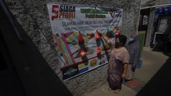 Warga mengambil paket sembako yang digantung di salah satu dinding di kampung Siaga COVID-19 di Kampung Rawa Pasung RW 22, Kota Baru, Kota Bekasi, Jawa Barat, Selasa (28/7/2020). [Suara.com/Angga Budhiyanto]