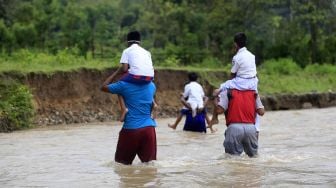 Seorang warga menggendong siswa Sekolah Dasar Negeri (SDN) 6 Tapa melintasi sungai Polanggua bersama sejumlah guru usai mengikuti pelajaran luar jaringan (luring) di Dusun III, Desa Langge, Tapa, Kabupaten Bone Bolango, Gorontalo, Rabu (29/7/2020). [ANTARA FOTO/Adiwinata Solihin]